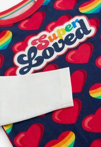 Puuvillane T-särk tumesinise taustaga, millel on punased südamed ja vikerkaarega "Super Loved" graafika. All on valged varrukate aktsendid.