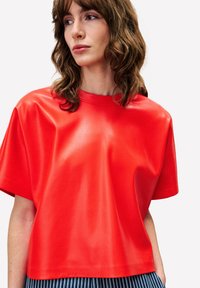 Rode korte mouw top van nep leer met een ronde hals, met een gladde, glanzende textuur en een losvallend ontwerp. Gestreepte broek zichtbaar eronder.