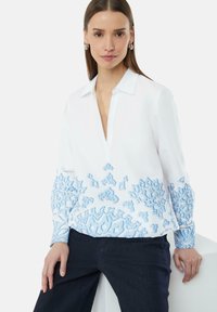 Witte shirt met een blauw geborduurd patroon op de mouwen en zoom, met een V-hals en een knoopsluiting van de kraag. Soepele stof, casual pasvorm.