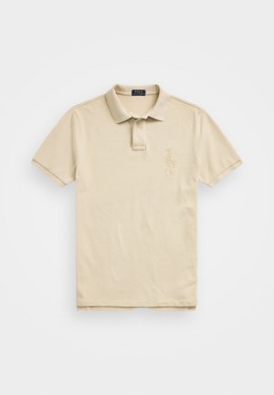 Beige polo shirt laget av bomull, med en krage med tre knapper, kortermet, og et brodert logo på venstre bryst. Glatt tekstur.
