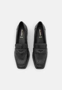 Mocassins en cuir noir avec une pointe carrée, des coutures décoratives et des clous argentés le long des bords. Intérieur rembourré noir.