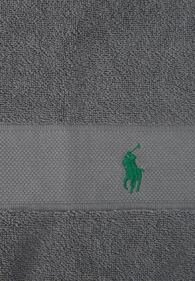 Γκρι πετσέτα με υφή και πράσινο κεντητό λογότυπο παίκτη πόλο στο κέντρο μιας λείας, διακοσμημένης λωρίδας.
