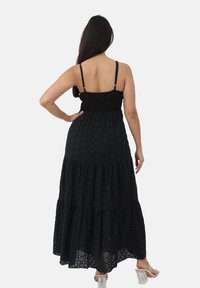 Sorte maxi kjole med smocked bodice, spaghetti stropper, lagdelt nederdel og struktureret stof med et subtilt mønster.
