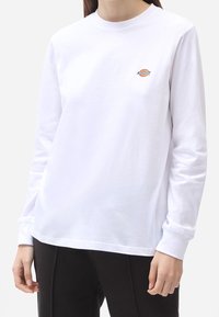 White long-sleeve t-shirt made of cotton, featuring a small colorful logo on the chest, with a crew neckline and relaxed fit.