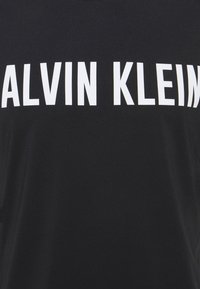 Černá tkanina s velkým bílým textem "CALVIN KLEIN" tištěným uprostřed.