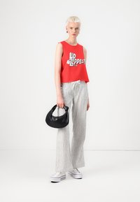 Red cropped tank top with "Led Zeppelin" graphic, gray striped wide-leg pants, and a black handbag. White sneakers complete the outfit.