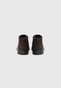 Bottines en daim marron avec une semelle plate en caoutchouc noir. Bout rond et panneaux latéraux élastiques pour un enfilage facile. Design minimaliste sans embellissements.