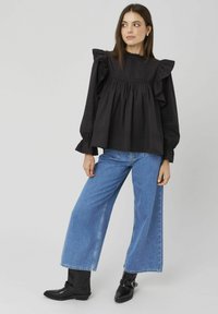 Blouse noire à manches volantées avec des détails texturés, associée à un jean bleu à jambes larges et des bottines noires. Design simple et moderne.