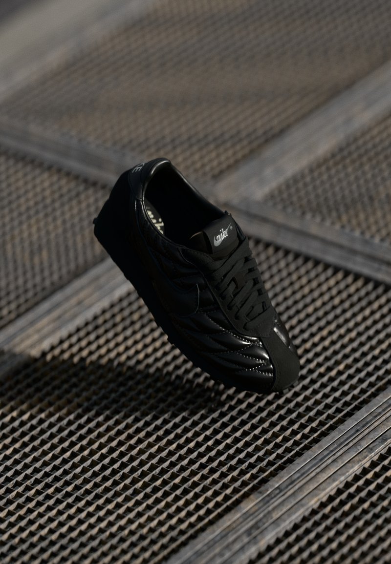 Črne teniske z zgornjim delom iz teksturirane usnjene površine, z gladkim nosom, vezalkami in logotipom na ježku. Povišane nad vzorčasto površino.