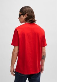 Camiseta de algodón roja con mangas cortas, un escote redondo y la parte trasera sin adornos. La tela parece suave con una textura lisa.