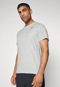 T-shirt grigio a maniche corte realizzato in un tessuto morbido, con un sottile logo Nike nero sulla spalla sinistra. Design semplice, vestibilità regolare.
