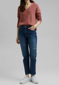 Pull en rose poussiéreux côtelé avec décolleté en V, associé à un jean bleu légèrement usé et des baskets blanches à lacets. Tenue décontractée.