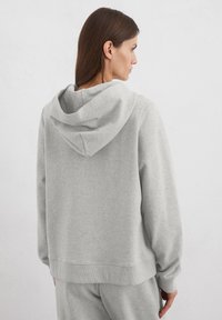 Grijze hoodie met een losse pasvorm, verstelbare capuchon, ribbelboorden en onderrand. Zacht materiaal met zijnaad, minimale stikseldetails.