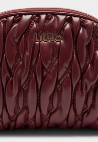 Plüschige burgunderrote Clutch-Tasche mit gestepptem Design, erhabenem Logo und strukturiertem Leder-Finish. Goldfarbener Reißverschluss entlang der Oberkante.