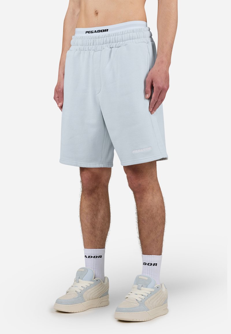 Lys blå, knæ-lange shorts lavet af blødt stof med elastisk talje. Har et logo på den nederste søm og en afslappet pasform.