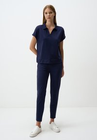 Navyblauw poloshirt met korte mouwen en V-hals, gecombineerd met een bijpassende set taps toelopende broek, beide gemaakt van zachte stof, gedragen met witte sneakers.
