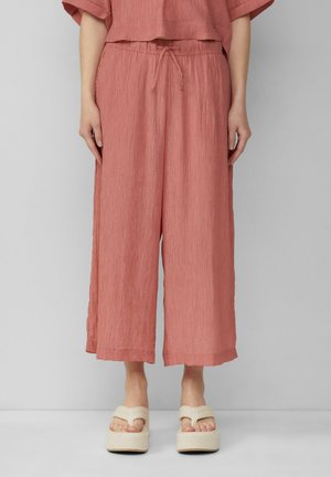 Pantalons larges rose texturés avec une taille élastique et un cordon de serrage. Associés à des sandales compensées de couleur beige clair.