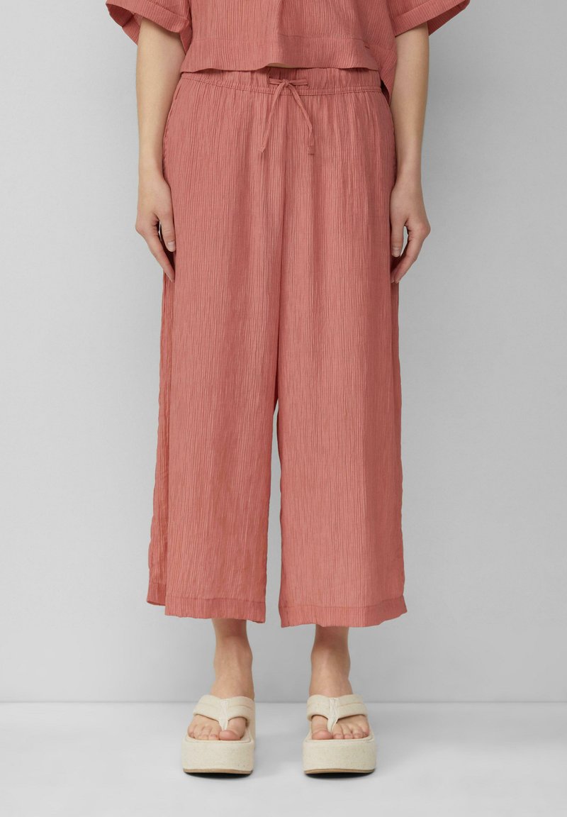 Roze, getextureerde wijde broek met een elastische tailleband en trekkoord. Gepaard met platform sandalen in een lichtbeige kleur.
