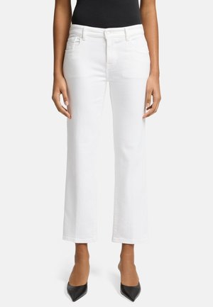 Pantalons en denim blanc à jambe large avec une taille haute, poches avant et finition nette. Associés à des talons aiguilles noirs.