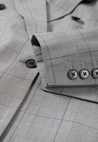 Tela de traje a cuadros gris con un tejido texturizado y botones negros. El patrón incluye detalles de cuadros finos y un acabado suave.