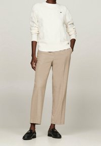 Biały sweter w splot warkoczowy z prążkowanym dołem, beżowe eleganckie spodnie i czarne loafersy z złotymi akcentami. Casualowy strój w kontrastujących kolorach.