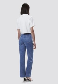 Camisa blanca corta con mangas cortas, combinada con jeans de mezclilla de tiro alto en azul claro que tienen bolsillos traseros y un corte holgado.