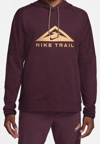 Sweat à capuche Nike Trail couleur bordeaux avec un logo triangulaire doré, capuche à cordon et poignets côtelés. Tissu lisse avec une coupe décontractée pour un confort optimal.