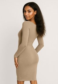 Beżowa, długa sukienka bodycon z okrągłym dekoltem, gładką teksturą, dopasowanym krojem, do kolan, podkreślająca talię i biodra.