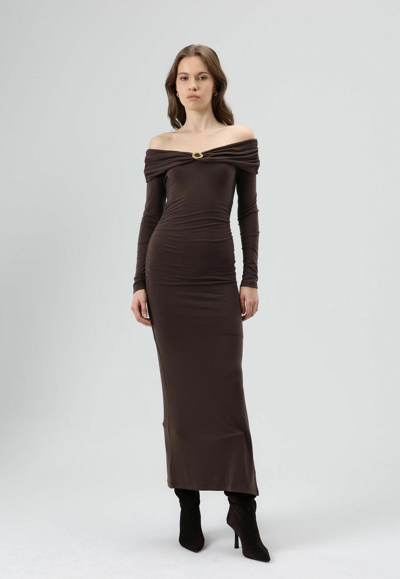 Bruine off-shoulder jurk met lange mouwen, geplooide details en een gouden accent bij de halslijn. Vloerlengte, aansluitend model.