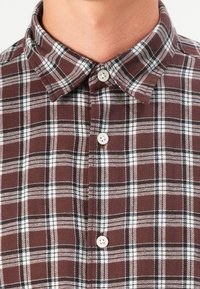 Brown and white plaid shirt with a button-down collar, featuring a soft fabric texture and a row of white buttons down the front.