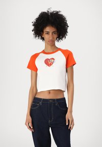 White crop top with orange raglan sleeves, featuring a colorful graphic of a character with an umbrella on the front. Dark blue denim pants.