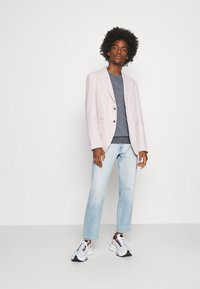 Light pink blazer with notched lapels and two buttons, gray sweater, light blue straight-leg jeans, and white sneakers with black accents.