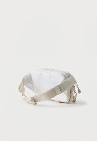 Λευκή και μπεζ υφασμάτινη τσάντα μέσης με ρυθμιζόμενο ιμάντα και δύο φερμουάρ, τοποθετημένη σε απλό ανοιχτόχρωμο φόντο.