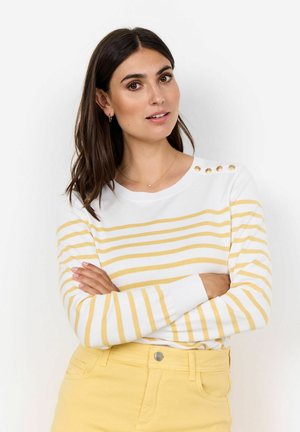 Witte trui met gele horizontale strepen, voorzien van decoratieve gouden knopen op de linkerschouder. Gekozen in combinatie met gele broek, met een gladde textuur.