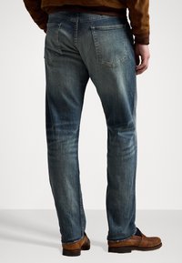 Modré džíny z denimu se střihem rovného fitu, s jemným vyblednutím, dvěma zadními kapsami a subtilním texturovaným povrchem, v kombinaci s hnědými botami.