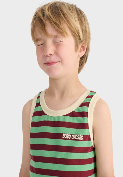 Jeune garçon aux yeux fermés et léger sourire, portant un débardeur rayé vert et bordeaux avec le texte « BOBO CHOSES ».