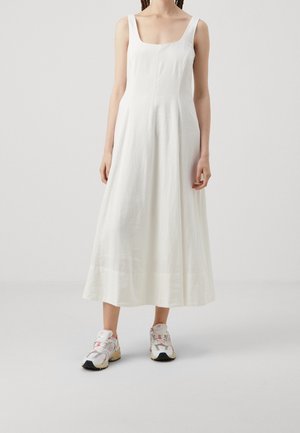 Vestito bianco senza maniche con scollatura quadrata, realizzato in un tessuto leggero, che scende fino a metà polpaccio, abbinato a scarpe da ginnastica colorate e sportive.