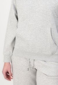 Hanorac gri cu mâneci lungi și manșete canalate, având un buzunar frontal și o croială lejeră. Asortat cu pantaloni cu șnur de același model.