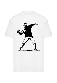 T-shirt bianca in cotone con una grafica in stencil nera di una persona che lancia un oggetto, evidenziando il contrasto e un design audace.