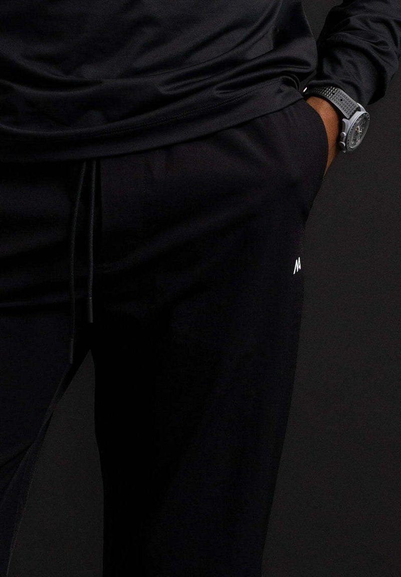 Zwarte sportbroek met een trekkoord in de taille, voorzien van een slim fit, een gladde textuur en een klein wit logo aan de zijkant.
