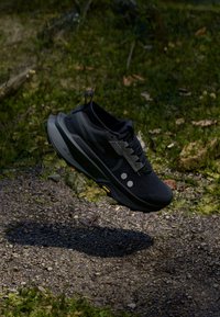 Black athletic shoe with cushioned sole, mesh upper, and reflective accents. Features a streamlined design and textured laces for secure fit.