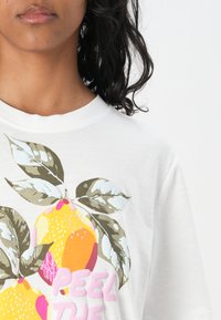 Hvid bomulds t-shirt med et farverigt citron grafisk design, grønne blade og pink tekst som skriver "PEEL THE" i en legesyg skrifttype.