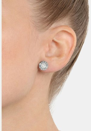Pendientes de aro de plata con forma redonda, un centro texturizado y el nombre de la marca grabado, acentuados con pequeñas piedras preciosas transparentes.