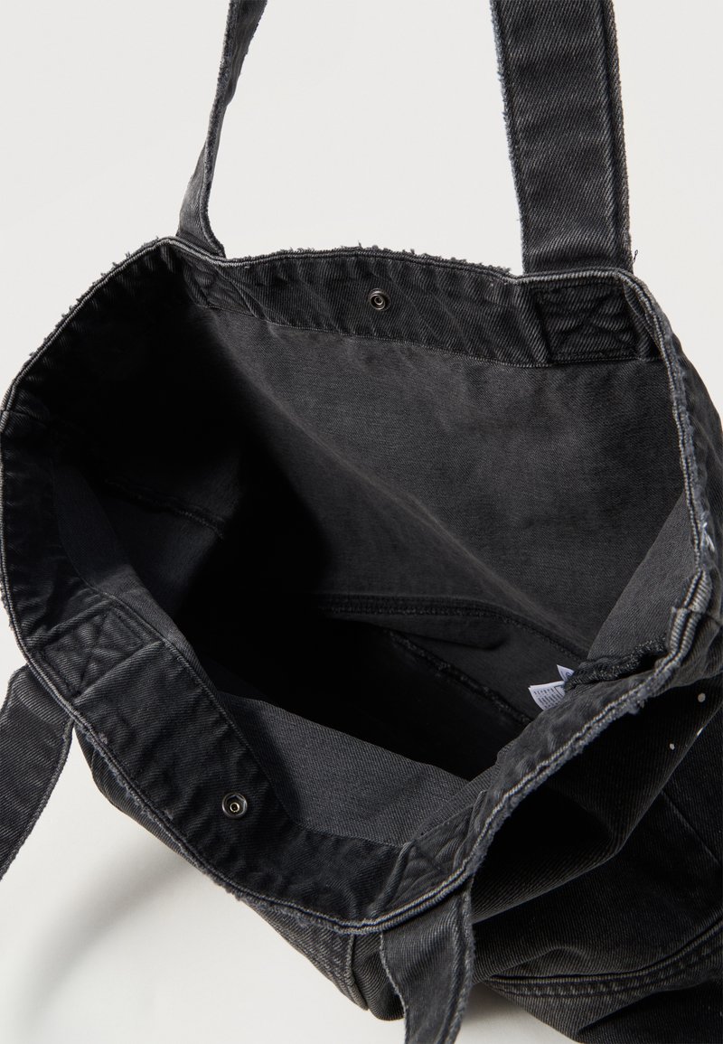 Schwarze Stofftragetasche mit langen Trägern, offenem oberen Teil mit Druckknopf, zeigt leeren Innenraum und genähte Nähte.