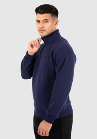 Sudadera blu navy con colletto alto e design con mezza zip. Presenta polsini e orlo a costine, realizzata in morbido tessuto testurizzato. Logo sul petto.