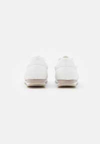 Weiße Sportschuhe aus einem glatten, lederähnlichen Material; niedriges Profil; auffälliger beiger Absatz; minimalistische Konstruktion.
