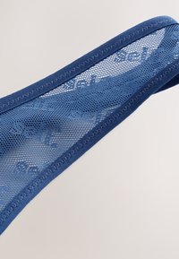 Tirante de sujetador azul de malla con un borde de tela lisa y sólida, decorado con costuras en zigzag. El tirante es semi-transparente, mostrando un patrón delicado.