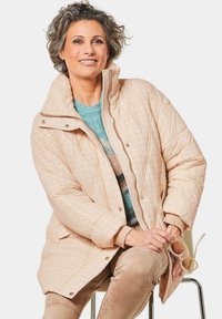 Gepolsterte, hellrosa Pufferjacke mit hohem Kragen, Reißverschluss und Druckknopfverschluss. Sie verfügt über ein strukturiertes Muster und gerippte Bündchen.