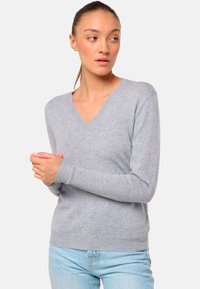 Hellgrauer V-Ausschnitt-Pullover mit langen Ärmeln und gerippten Bündchen. Strickstruktur, schlanker Schnitt und weicher Stoff. Getragen über hellblauen Jeans.