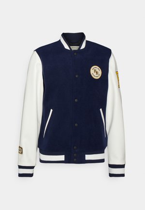 Giacca varsity blu navy con maniche bianche, polsini e orlo a righe, bottoni automatici, due tasche frontali e patch ricamati su petto e maniche.